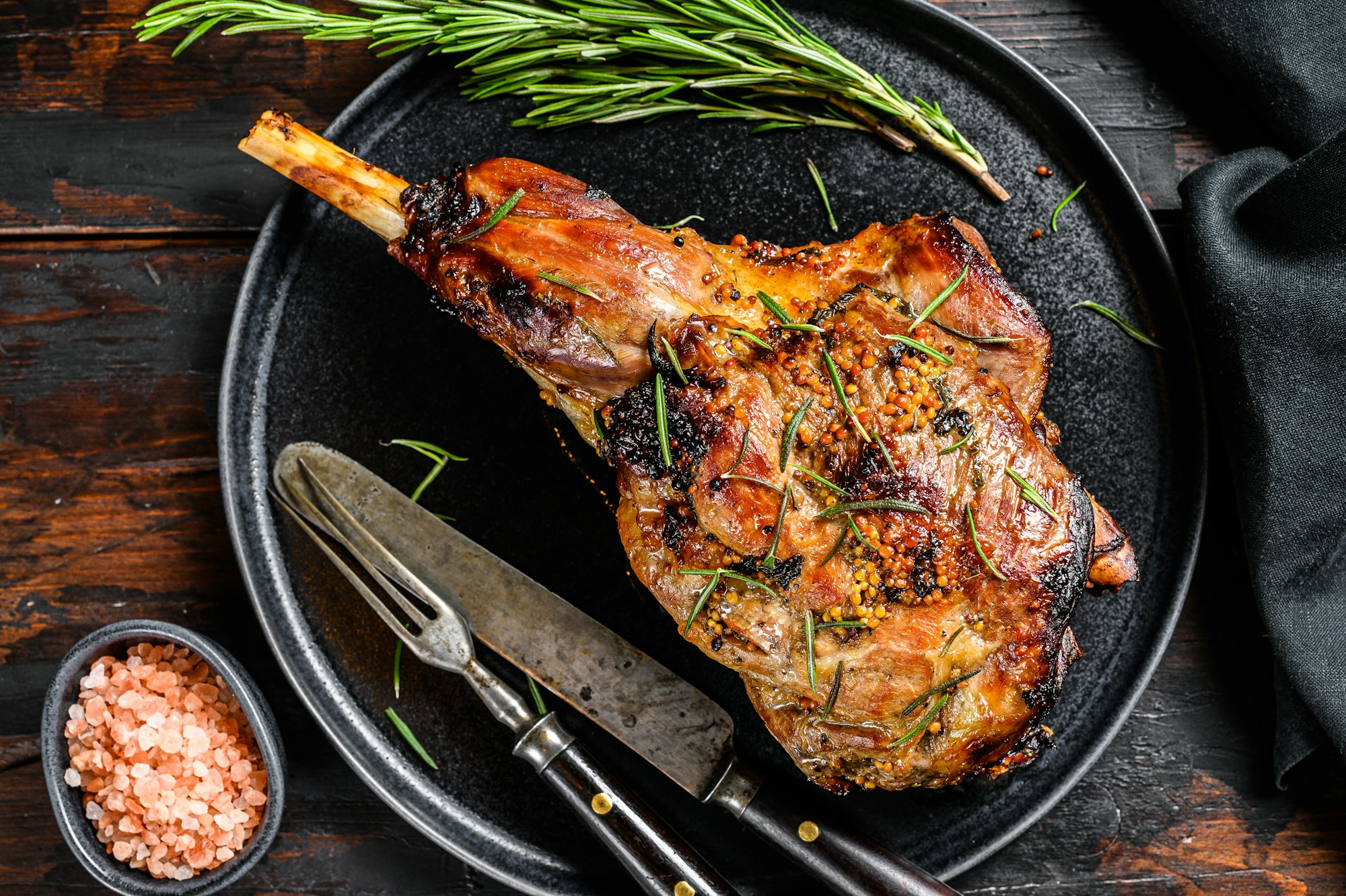 Baked lamb, sheep leg with rosemary. Dark wooden background. Top view