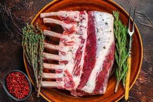 Raw fresh rack of lamb with green herbs. Dark background. Top view